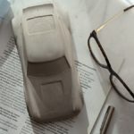 A model car, eyeglasses, and pen on a newspaper.