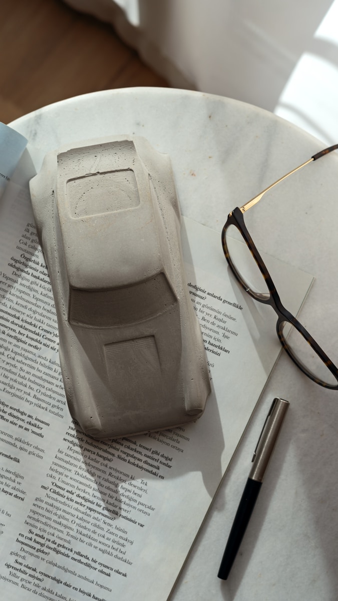 A model car, eyeglasses, and pen on a newspaper.